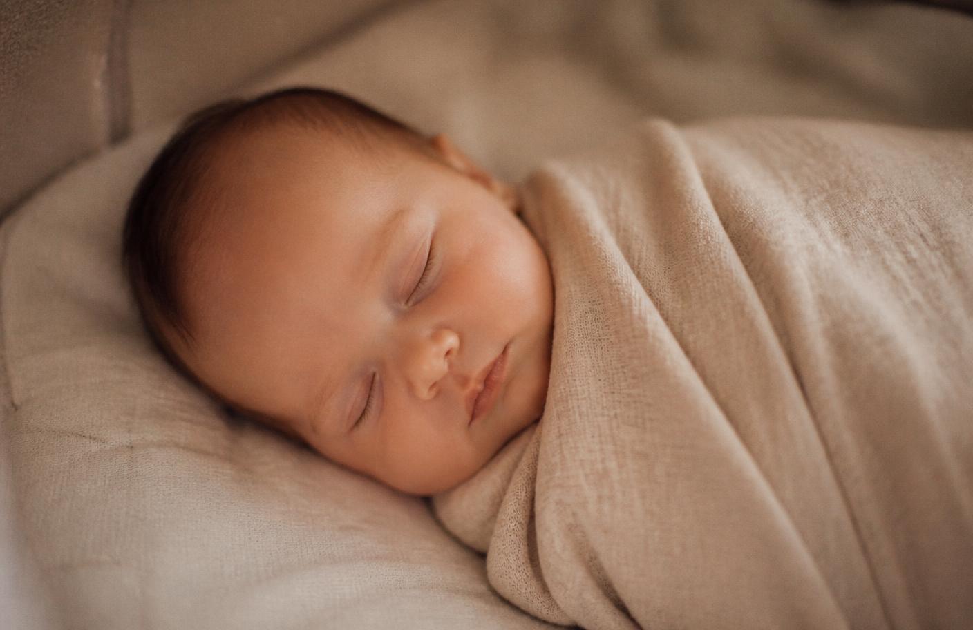 A newborn sleeping peacefully swaddled in soft beige muslin